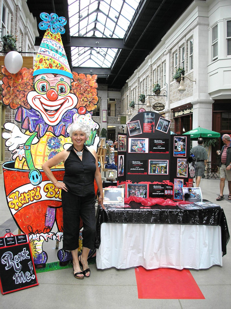 Dorothy Amey posing in front of Drawing Attention booth for Art in the Street in Guelph.